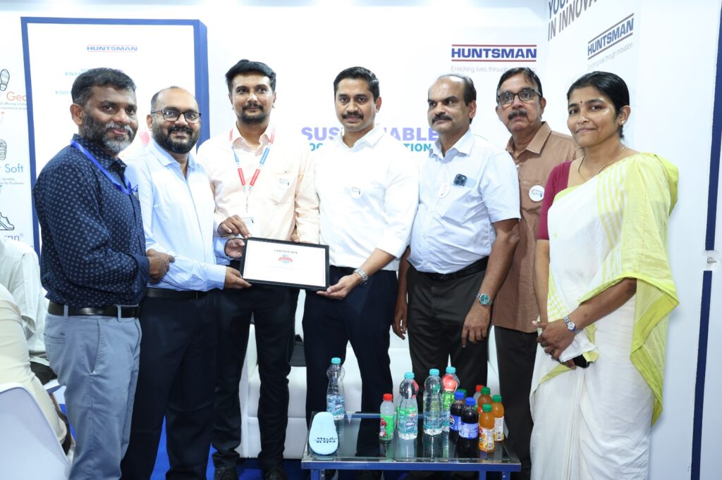 A group at the Huntsman stand at a trade fair, with a supplier rating certificate held up at the centre